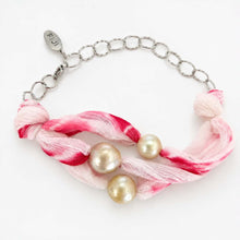 Load image into Gallery viewer, A silver chain bracelet with a knotted pink and white striped fabric centerpiece, accented by three round pearls. The tag on the clasp is engraved with 'FIJI'.