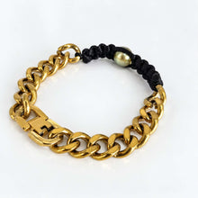Load image into Gallery viewer, A gold-toned chunky curb chain bracelet with a black braided cord closure and a small round pearl accent bead, shown on a clean white background.