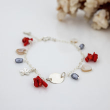 Load image into Gallery viewer, A silver bracelet with red coral and mother of pearl beads, featuring a frangipani charm, displayed alongside a piece of coral.