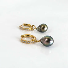 Load image into Gallery viewer, A pair of gold huggie hoop earrings, each adorned with small clear pavé stones and featuring dangling pearls, set against a clean white background.
