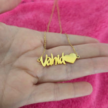 Load image into Gallery viewer, A gold nameplate necklace spelling 'Vahid' with a small heart, held in a person's hand against a bright pink textured background.