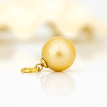 Load image into Gallery viewer, A single gold pendant charm shaped like a smooth, polished pearl with a small gold ring clasp, resting on a reflective white surface against a soft, out-of-focus cream background.