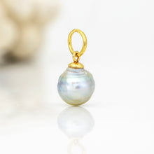 Load image into Gallery viewer, A pearl pendant charm with a polished gold-tone loop and cap, resting on a reflective white surface.