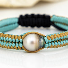 Load image into Gallery viewer, A close-up of a braided bracelet featuring light blue and tan woven cords, a central iridescent white pearl, and a black woven section in the background.
