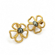 Load image into Gallery viewer, A pair of gold flower-shaped earrings with textured edges and a dark gray oval pearl set in the center, shown on a plain white background.
