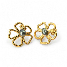 Load image into Gallery viewer, A pair of gold flower-shaped stud earrings with textured petals and a dark gray oval pearl set in the center, shown on a plain white background.
