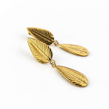 Load image into Gallery viewer, A pair of gold dangle earrings designed as textured leaf charms, shown on a clean white background.

