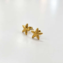 Load image into Gallery viewer, A pair of gold starfish stud earrings with a textured surface, displayed on a clean white background.
