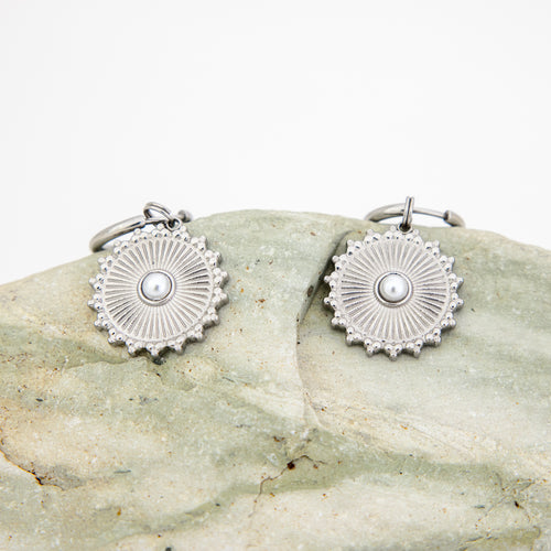 Silver earrings with a central pearl on a stone surface