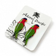 Load image into Gallery viewer, A pair of colorful parrot-shaped earrings displayed on a white branded card that reads 'Adorn Pacific' with a palm tree graphic. The earrings are bright green with red heads, yellow beaks, and dark blue/black tops, photographed on a clean white background.
