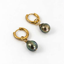 Load image into Gallery viewer, A pair of gold huggie hoop earrings with small clear stones along the front, suspending dark green-black pearls, shown on a clean white background.
