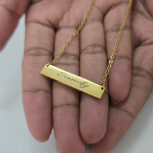 Load image into Gallery viewer, Gold necklace with a bar pendant engraved with 'Sandy' held in a hand.
