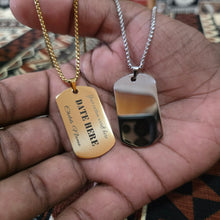 Load image into Gallery viewer, Two dog tag necklaces held in a hand, one gold-toned with engraved text and one silver-toned with a reflective finish, on chain straps.
