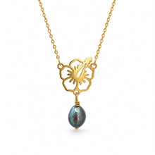 Load image into Gallery viewer, A gold-tone necklace featuring a cutout floral pendant with a hibiscus flower and a dangling teardrop-shaped iridescent blue-gray pearl, shown on a plain white background.
