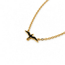 Load image into Gallery viewer, A gold chain necklace featuring a flying bird pendant with black enamel fill, photographed on a clean white background.

