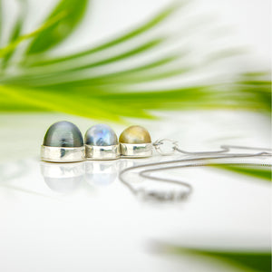Silver necklace with three gemstones against a blurred natural background