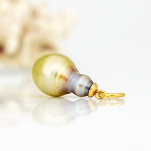 Load image into Gallery viewer, A single pearl pendant charm with a gold bail, resting on a reflective white surface with a soft, blurred decorative background.
