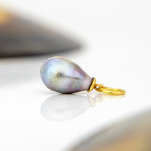 Load image into Gallery viewer, A teardrop-shaped iridescent pearl pendant with a gold bail, resting on a reflective white surface.
