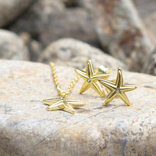 Load image into Gallery viewer, Starfish shaped earrings in gold a textured surface with blurred background
